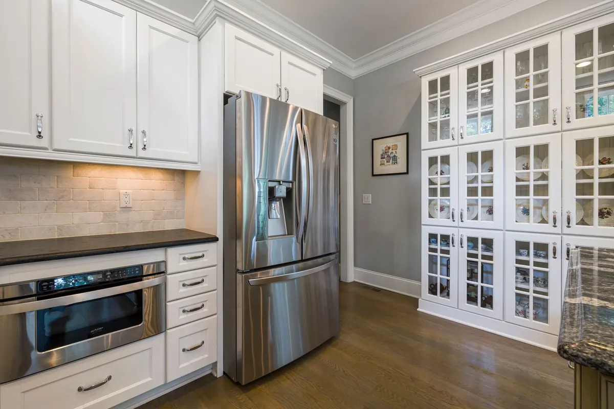 White shaker kitchen with glass-front cabinets and stainless refrigerator